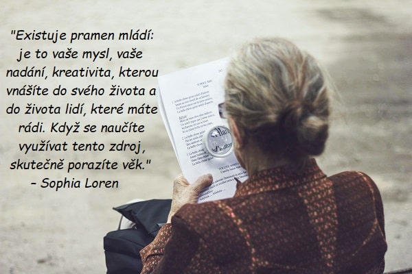 Stará žena čtoucí si noviny pomocí lupy s citátem pro staré od Sophie Loren.