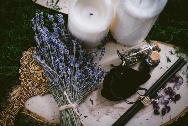 Fotografie čarodějnických předmětů – sušená levandule, pytlíček, hůlka, bylinky, zrcátko a svíčky na dřevěném kmeni. 