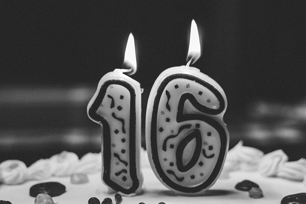 Černobílá fotografie s narozeninovým dortem a hořícími svíčkami ve tvaru číslic 1 a 6. 