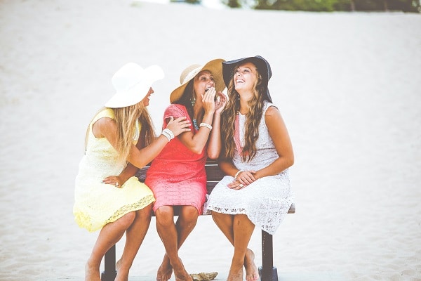 Tři smějící se ženy sedící na lavičce na pláži