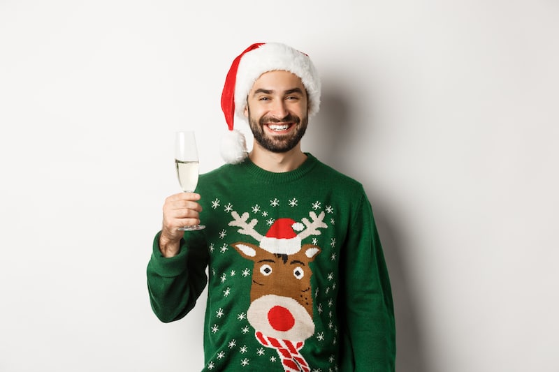 Muž ve vánoční čepici a svetru se sobem se vesele usmívá, zvedá přípitek.