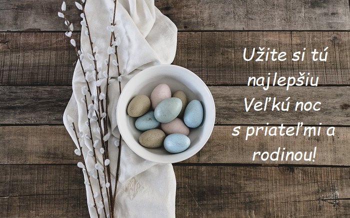 Barevná vajíčka v bílé misce s dekorací z kočiček na dřevěném pozadí se slovenským blahopřáním k Velikonocům.