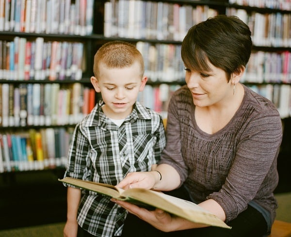 Žena, která předčítá malému chlapci v knihovně.