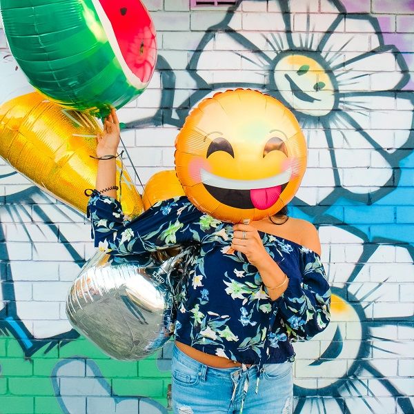 Žena držící před tváří balónek smějícího se emoji