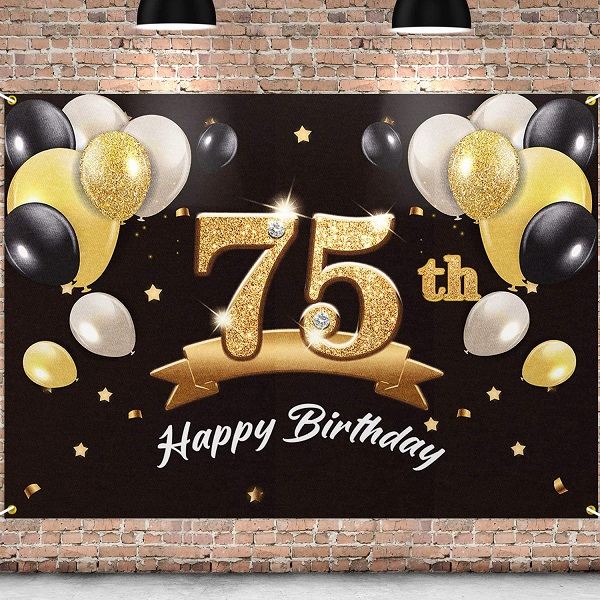 Zlatý nápis "75th Happy Birthday" na černém pozadí zdobeném zlatými a černými balónky a konfetami. 
