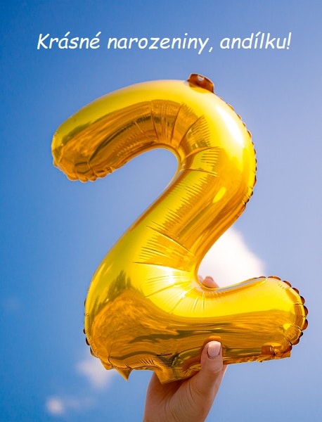 Ruka držící balónek ve tvaru čísla dvě na pozadí modré oblohy s přáním krásných narozenin. 