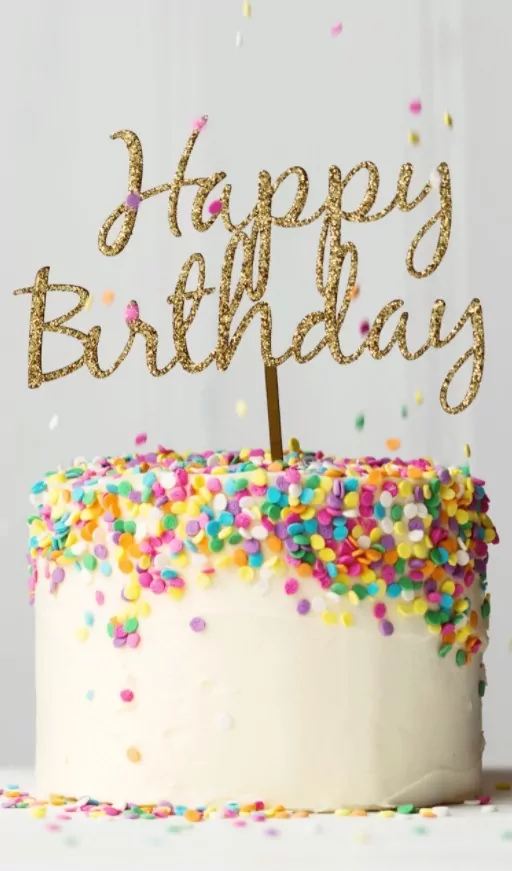 Narozeninový dort zdobený barevnými čokoládovými konfetami a se zlatým narozeninovým nápisem.
